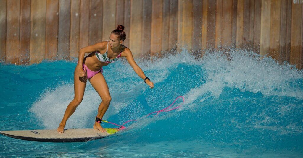 A woman skillfully rides a wave on a surfboard in a pool, showcasing water sports excitement.
