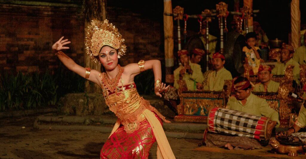Balinese dancer in vibrant attire performing a cultural dance with musicians in Bali, Indonesia.