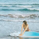 Woman with a surfboard enjoying a sunny day by the ocean, perfect summer vibes.