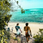 Surfers make their way down a lush path to a stunning beach in Bali, Indonesia.