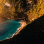 A breathtaking aerial view of Bali's cliffs and turquoise beach at sunset, highlighting nature's beauty.