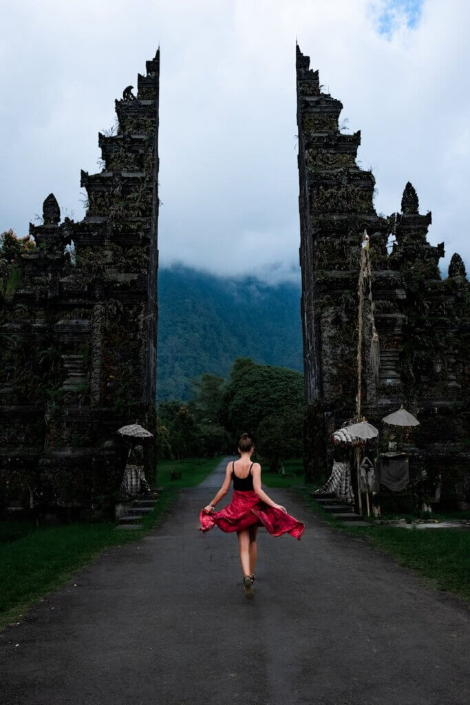 A woman twirls in a red dress at the famous Handara Gate in Bali, Indonesia, amidst misty mountains.
