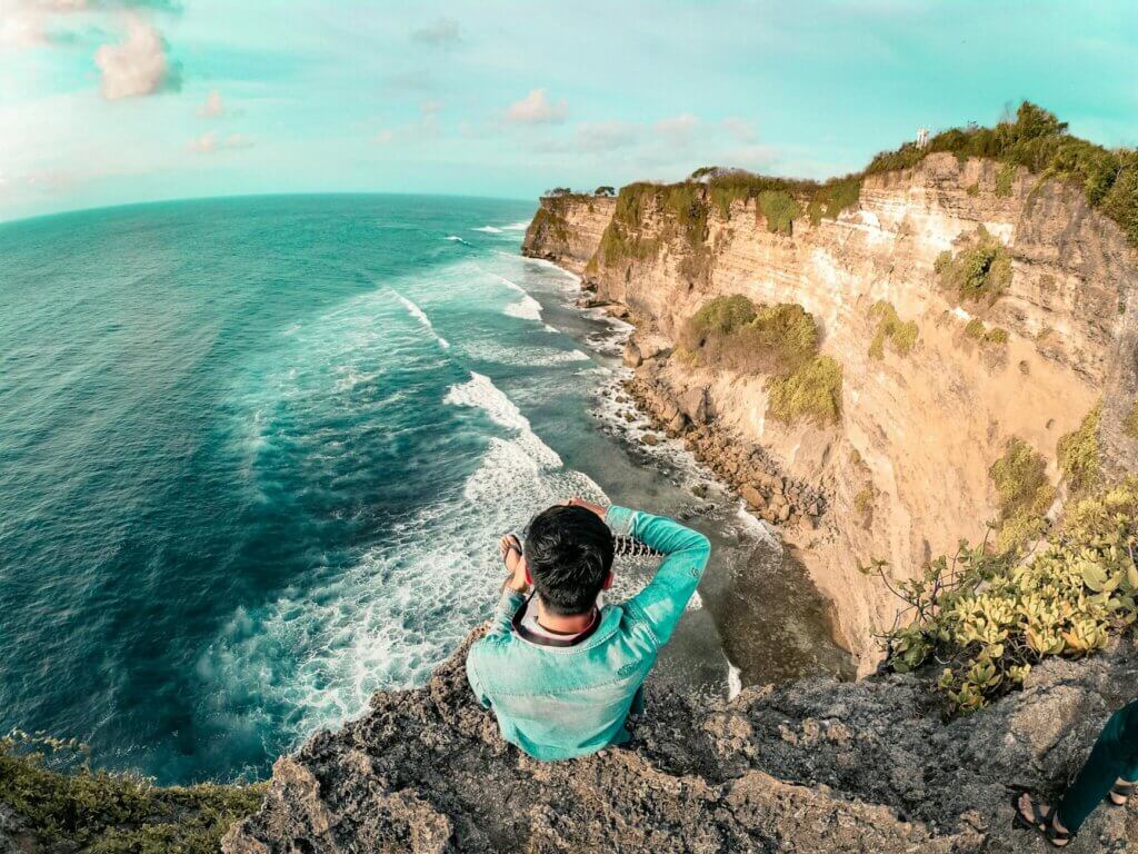 Man sitting on a cliff edge enjoying the ocean view in Bali. Perfect for travel and relaxation themes.