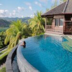 A woman relaxes in an infinity pool overlooking tropical scenery at a Bali villa.