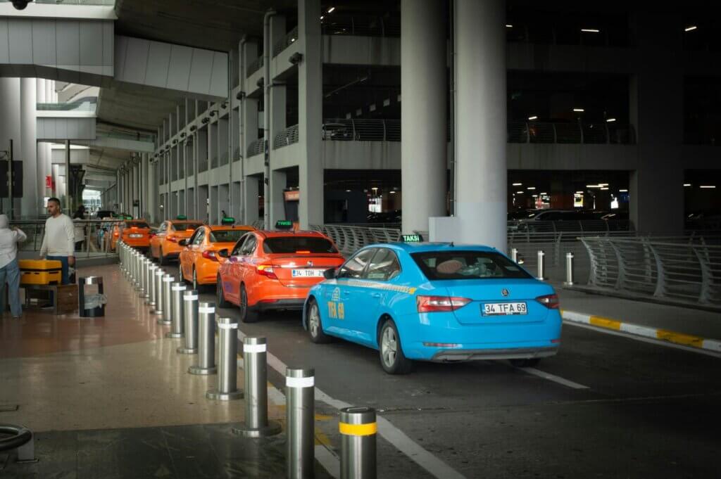 Vibrant taxis lined up at Istanbul Airport arrival terminal with passengers and drivers interacting.