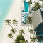 A stunning aerial view of a tropical beach resort with palm trees, turquoise waters, and white sand.