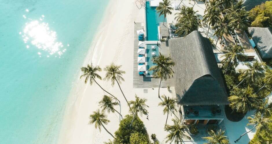 A stunning aerial view of a tropical beach resort with palm trees, turquoise waters, and white sand.
