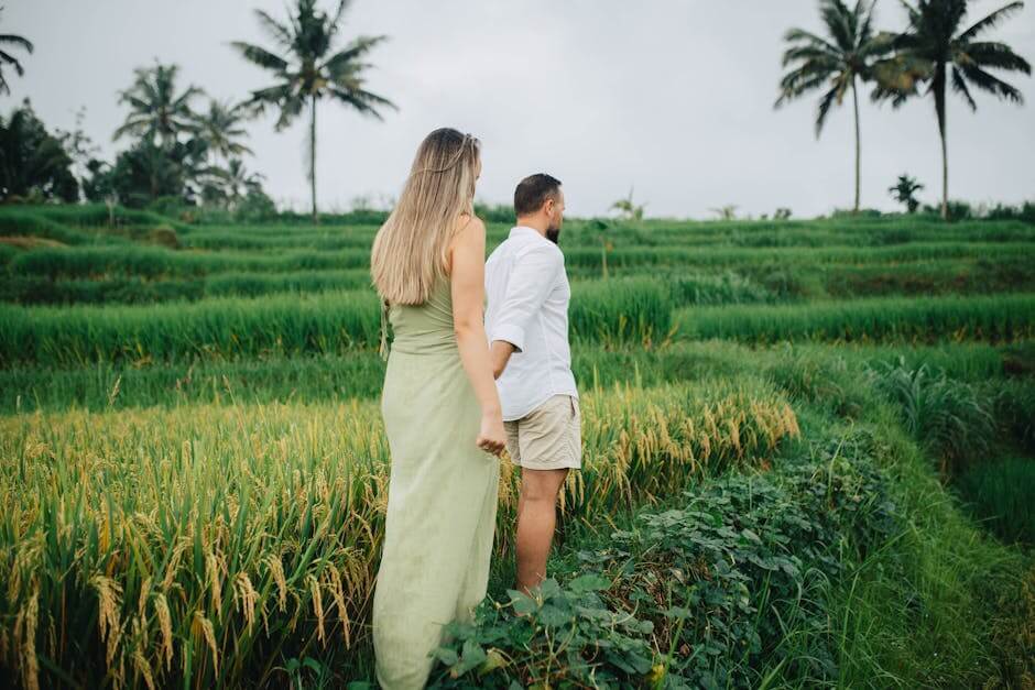 Couple walking among lush Balinese rice terraces holding hands, capturing serenity and nature.