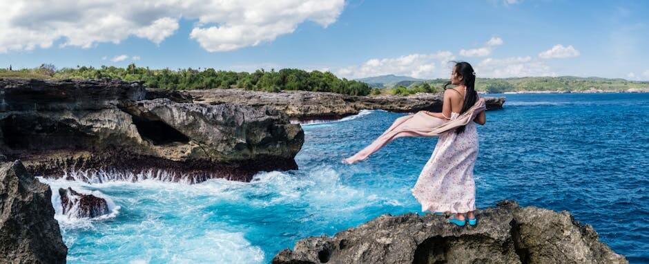 Woman in a flowing dress admiring the ocean view from a rocky cliff in Nusa Penida, Bali.