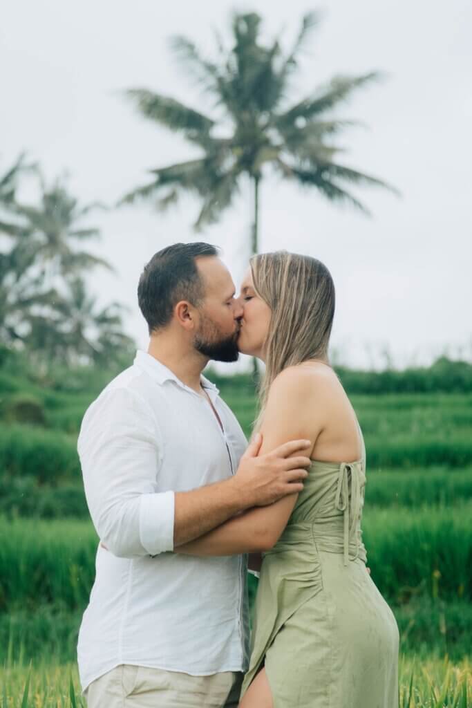 A couple sharing a kiss in a lush, tropical landscape with palm trees.